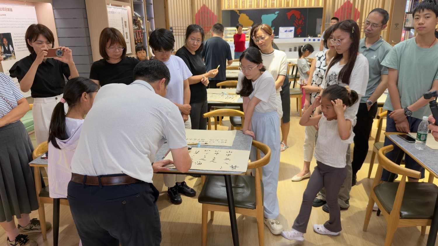 魏明老师现场伏案书写，老少围坐观看